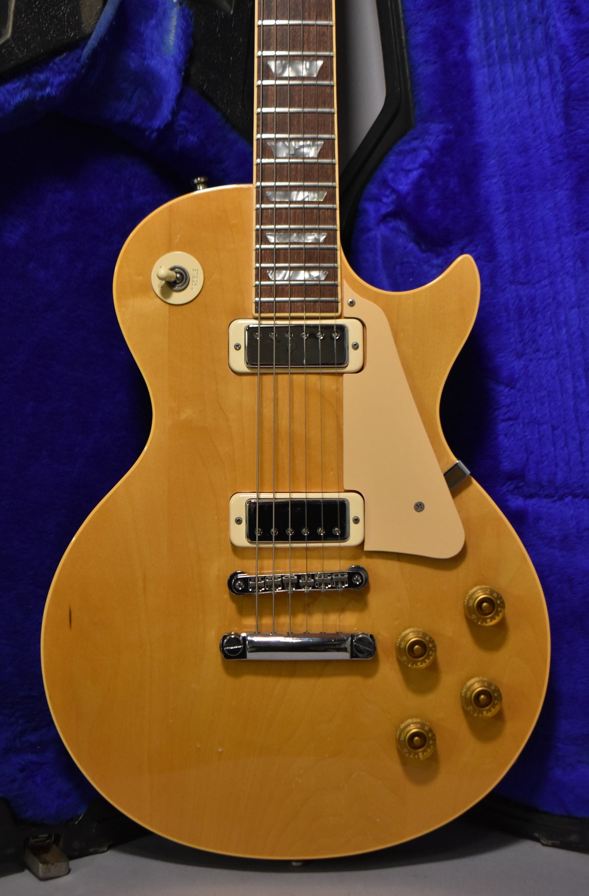 Full front view of a natural finish electric guitar with two humbuckers, a cream pickguard, and four amber control knobs.