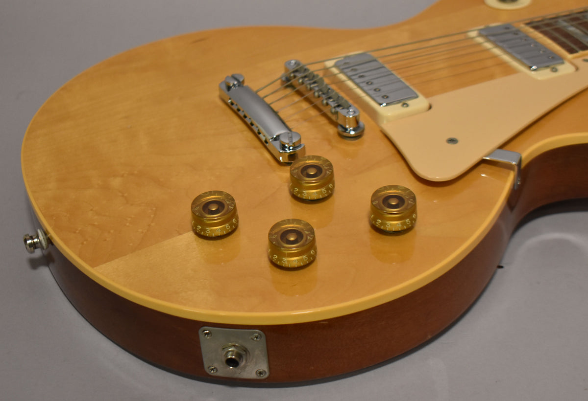 Close-up of the guitar's lower body, showing the natural finish, four gold top hat knobs, chrome bridge, and cream pickguard.
