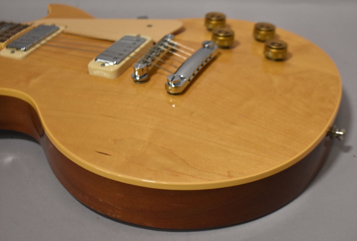 Close-up of the guitar body, showing the natural wood grain, chrome hardware, four amber control knobs, and some wear on the lower bout.