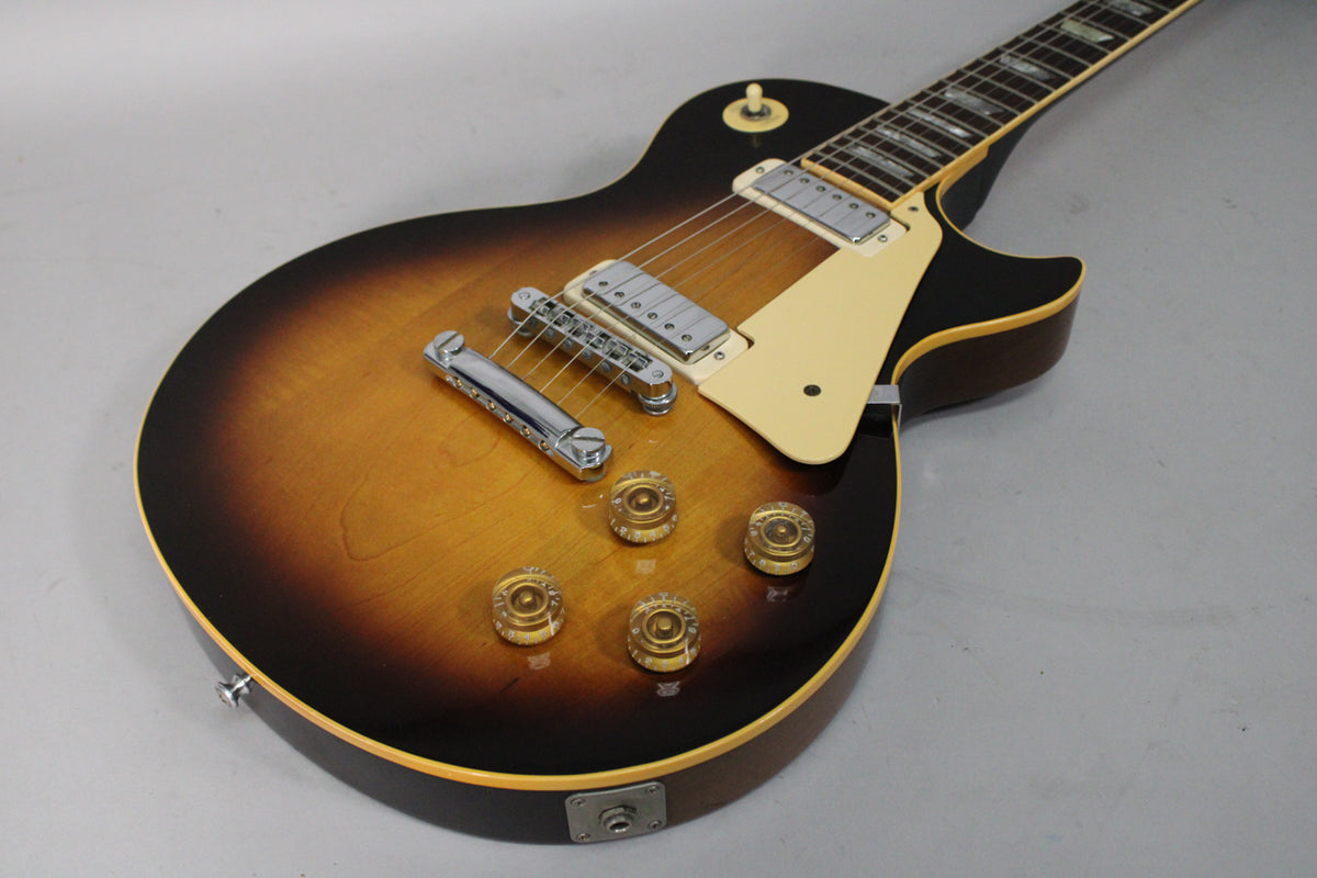 The tobacco burst body of the guitar is angled from the lower left, showing chrome hardware, cream pickguard, and four amber knobs.