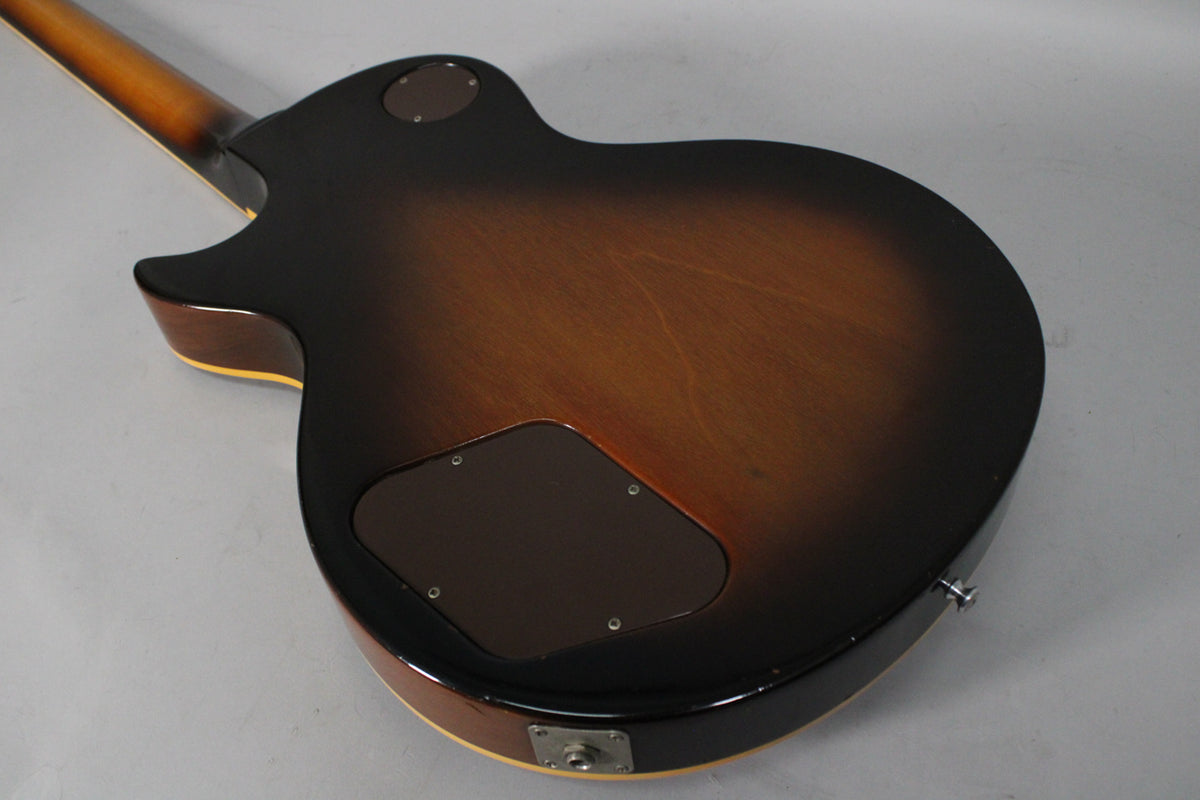 The back of a tobacco burst guitar, showing the neck joint, control cavity cover, and input jack with some wear.