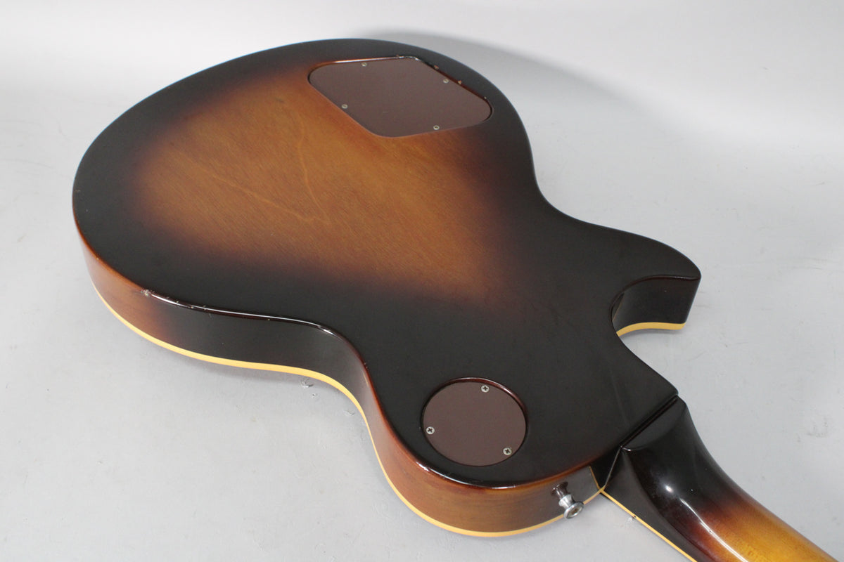 The back of a tobacco burst guitar, showing two brown control cavity covers and some finish wear on the body edge.