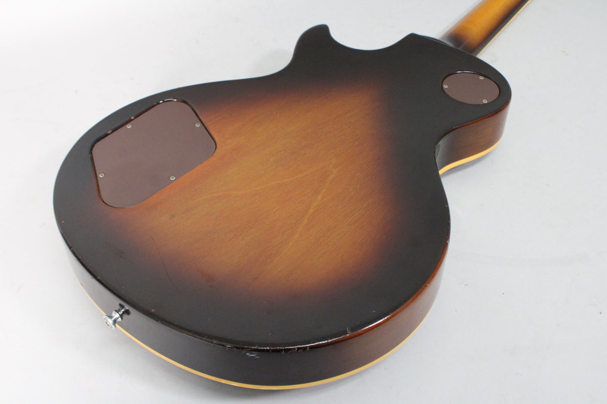 The guitar's tobacco burst back shows light scratches, a brown control cavity cover, and a strap button on the lower bout.