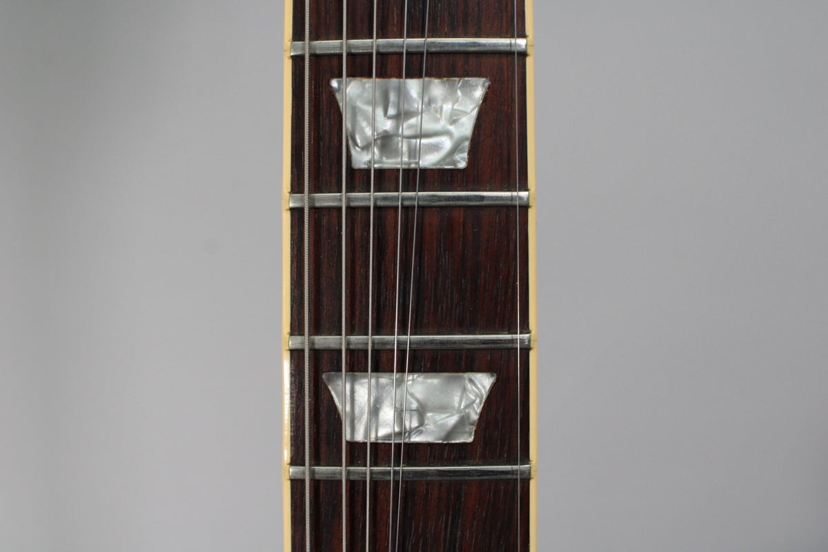 Close-up of the dark rosewood fretboard with trapezoid mother-of-pearl inlays, showing frets and strings, and cream binding.