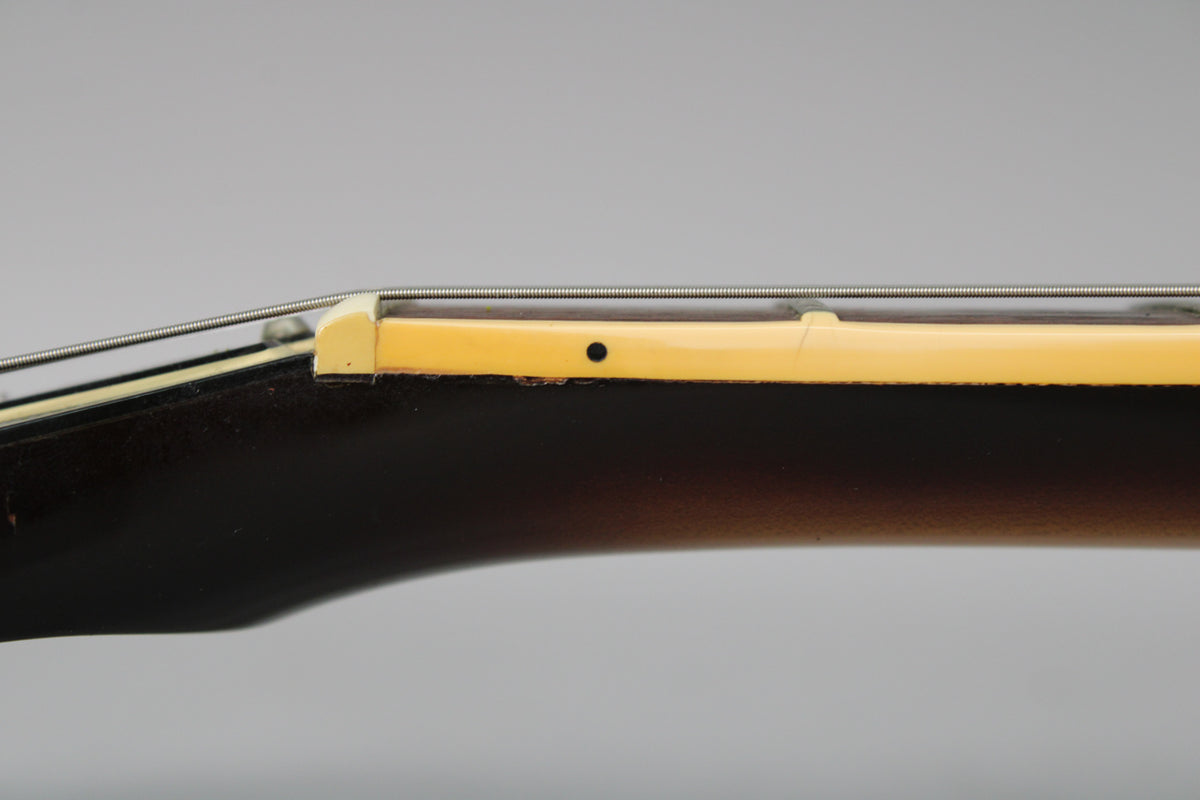 Close-up of the guitar's nut and first fret, showing a dark tobacco burst finish on the neck and light wear on the binding.