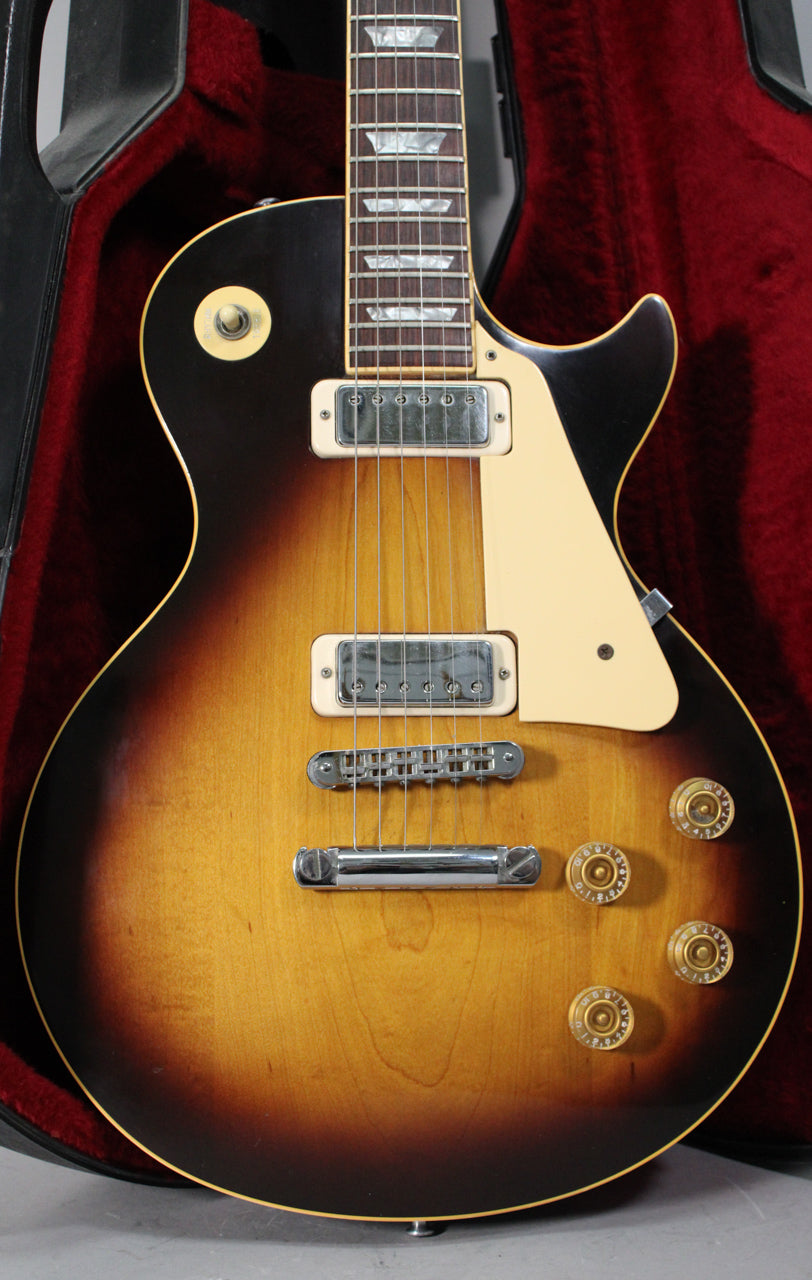 The tobacco burst guitar body is framed from the neck to the bottom, showing two humbuckers, a cream pickguard, and four gold control knobs.