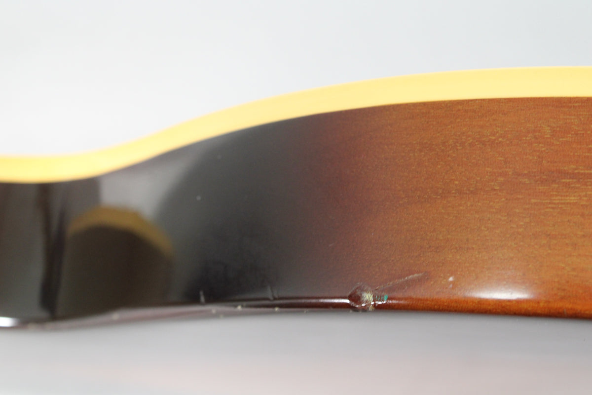 Close-up of the guitar's lower body edge, showing a tobacco burst finish with cream binding and a notable ding on the side.