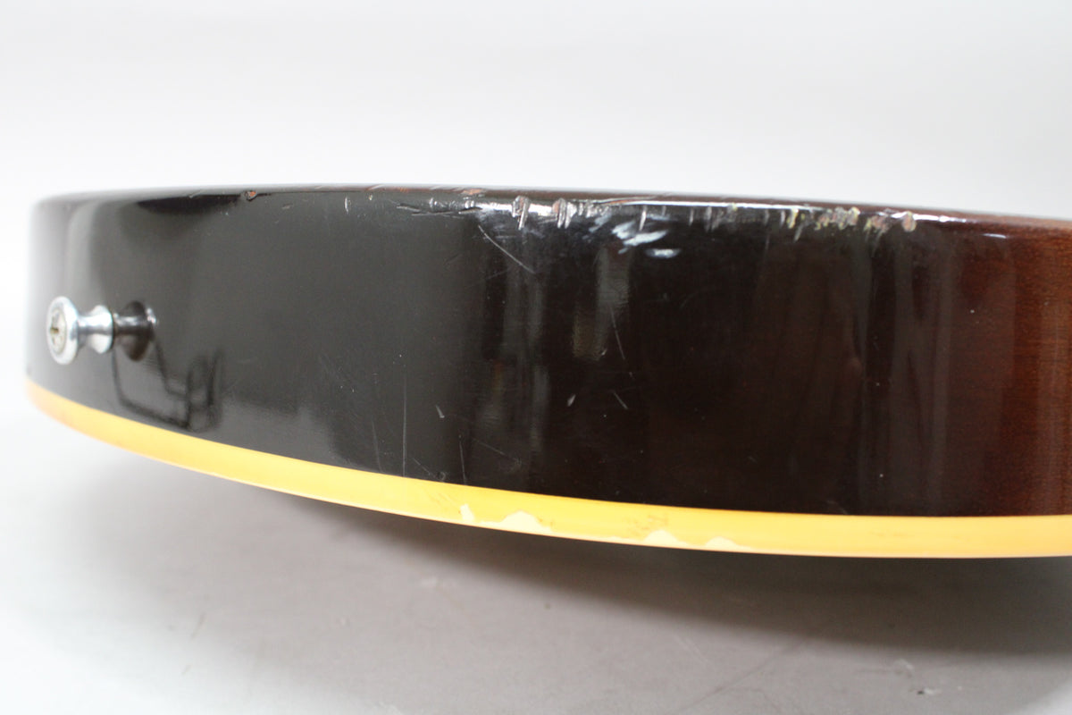 Close-up of the guitar's lower bout, showing the dark brown finish, cream binding, and heavy scratches and dings along the edge.