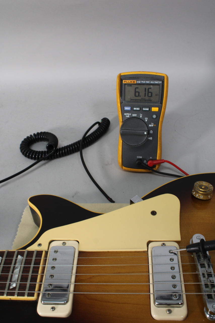 Close-up of the tobacco burst body and cream pickguard, with a multimeter showing 6.16 on the bridge pickup.