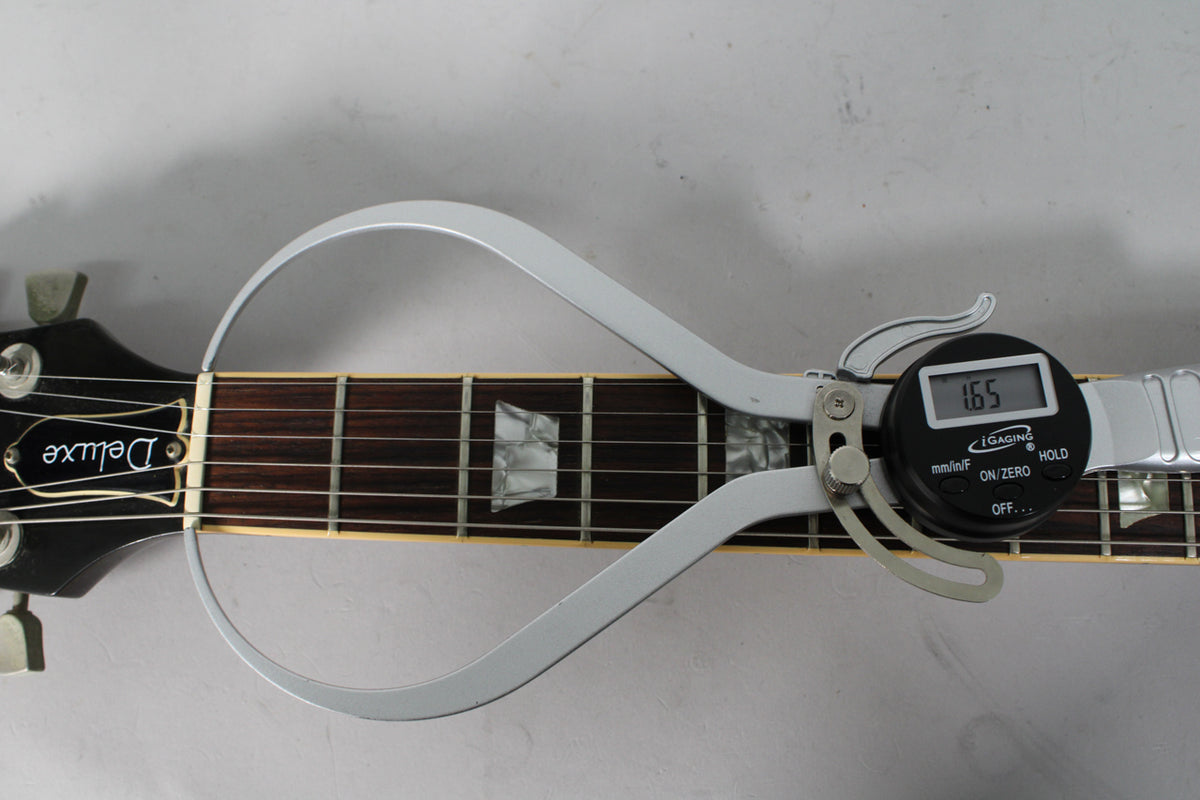 Overhead view of the guitar's dark headstock and rosewood fretboard, with a digital caliper measuring the nut width at 1.65 inches.