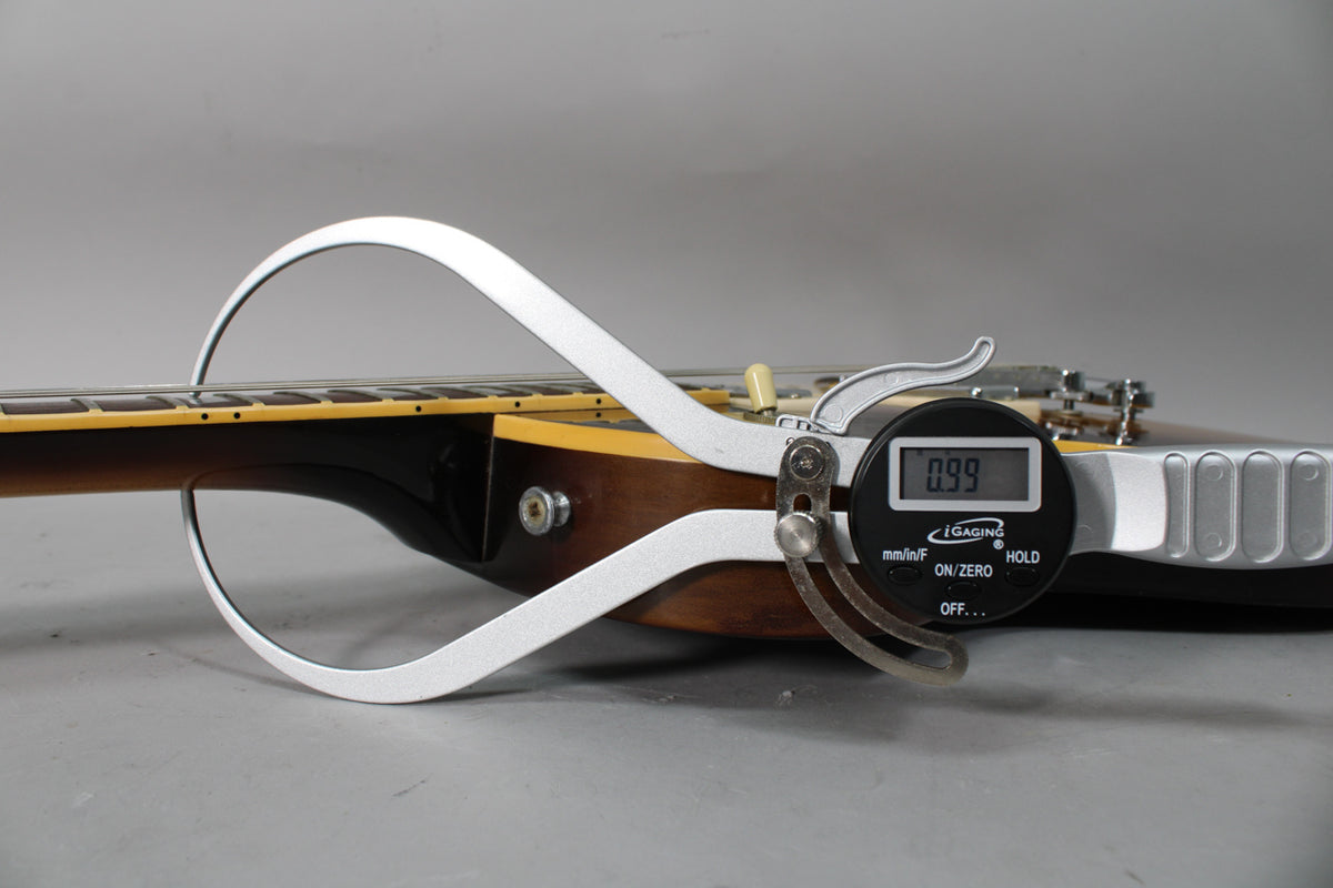 Close-up of the tobacco burst body and neck joint, with a digital caliper measuring the string height at 0.99mm.