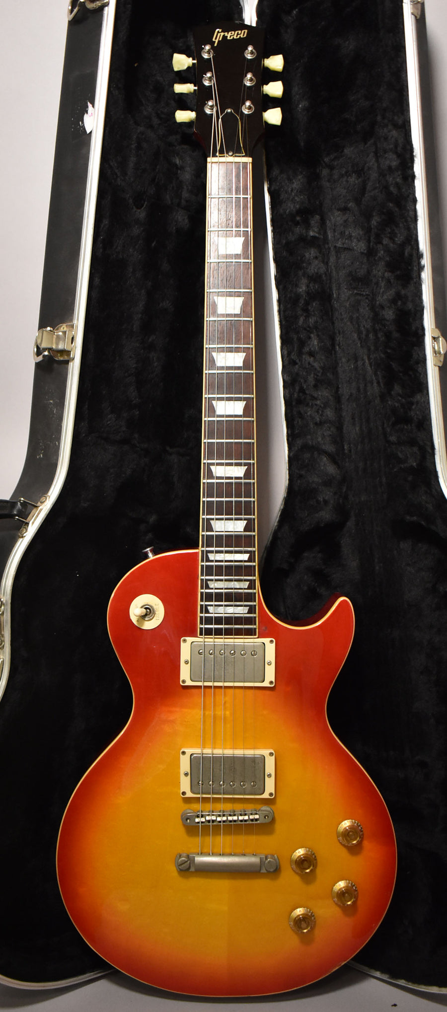 Full-length view of a sunburst guitar with cream binding, trapezoid inlays, two humbuckers, and four gold top hat knobs.