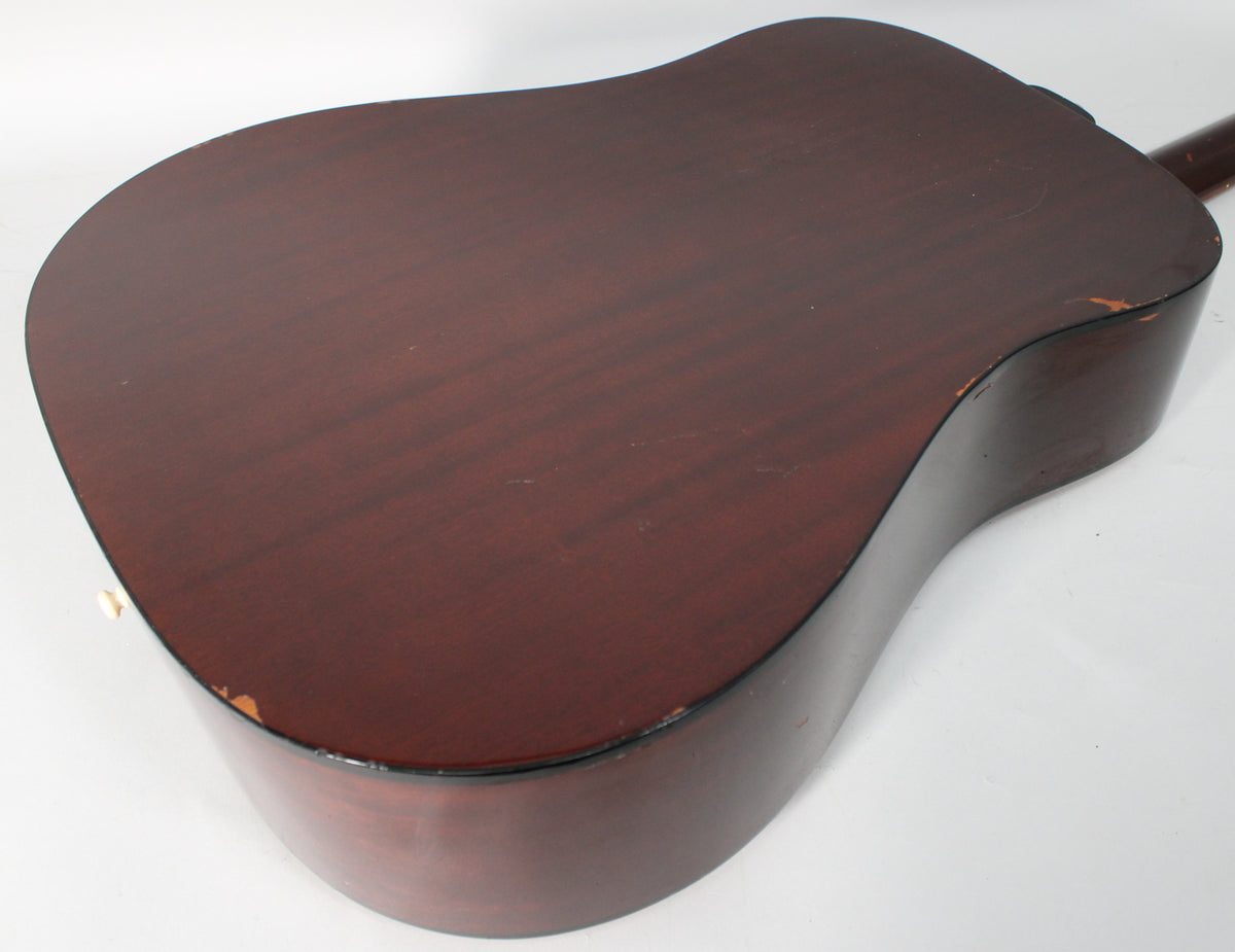 The back of the dark brown acoustic guitar is angled, showing wear and chips along the edges and a few light scratches on the surface.