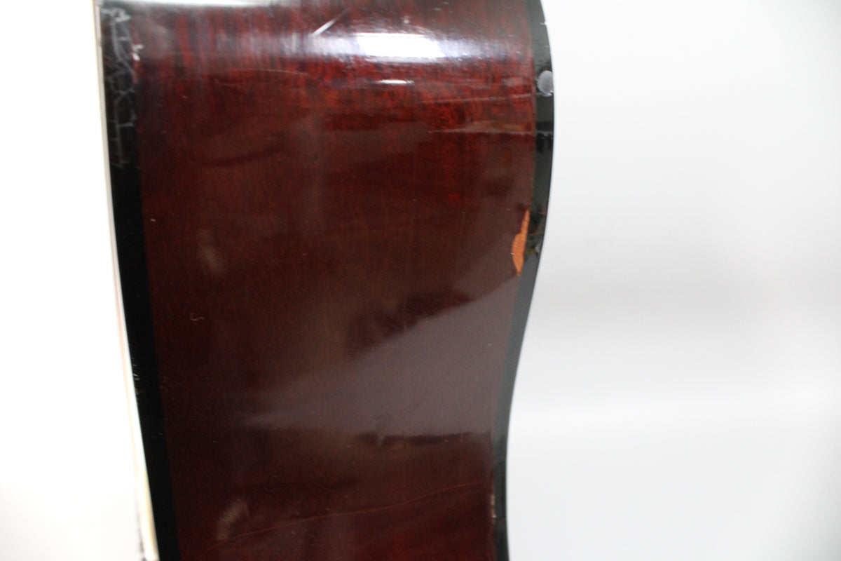 Close-up of the guitar's dark reddish-brown side, showing finish checking along the binding and a chip exposing lighter wood.