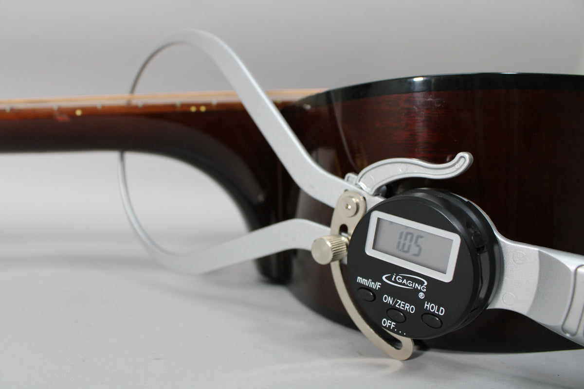 A digital caliper measures the dark brown acoustic guitar's neck thickness at 1.05 inches, showing light wear on the body.