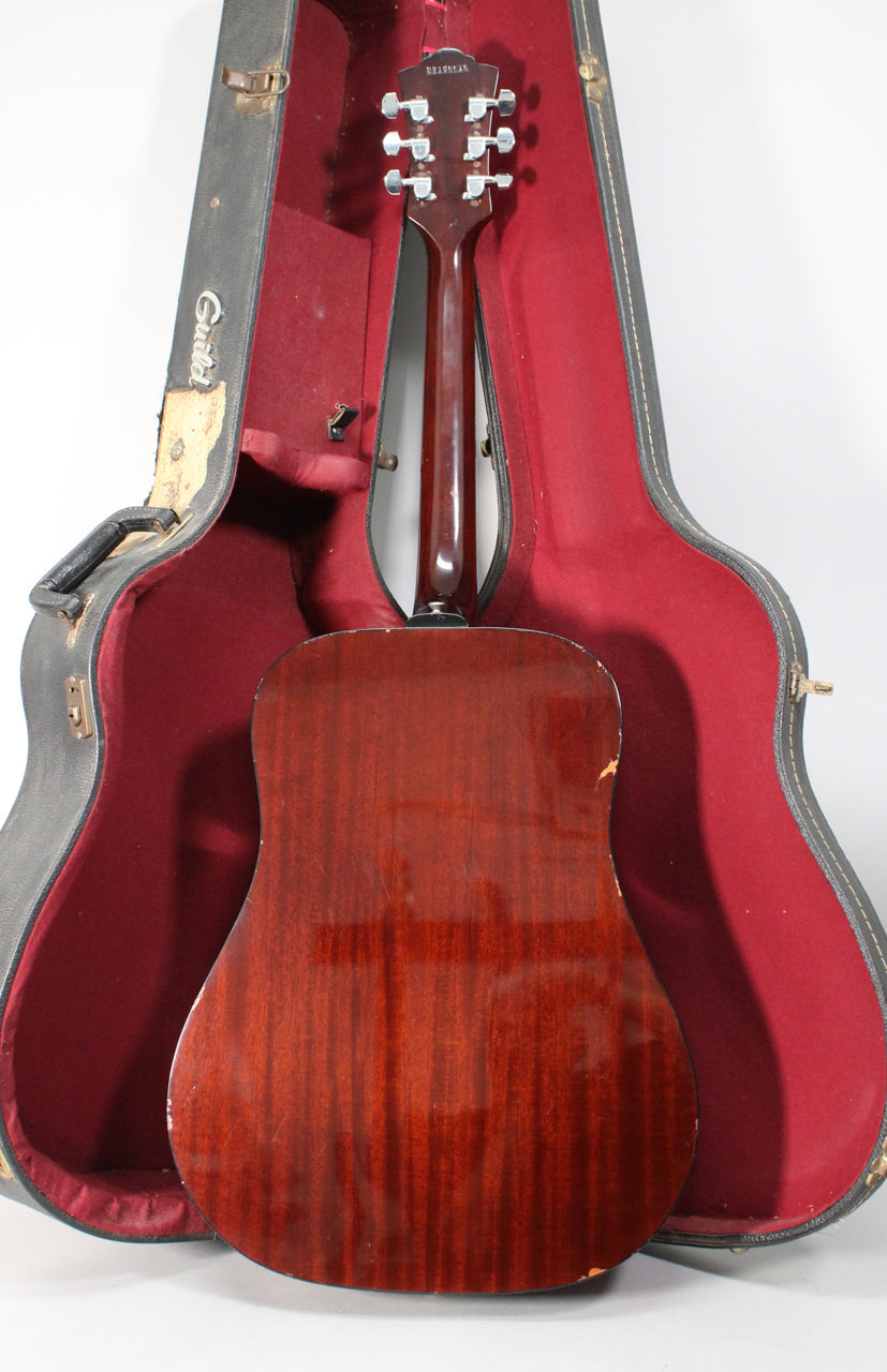 The guitar's dark reddish-brown back and neck are visible, with six chrome tuners and a worn black hard case with red lining.