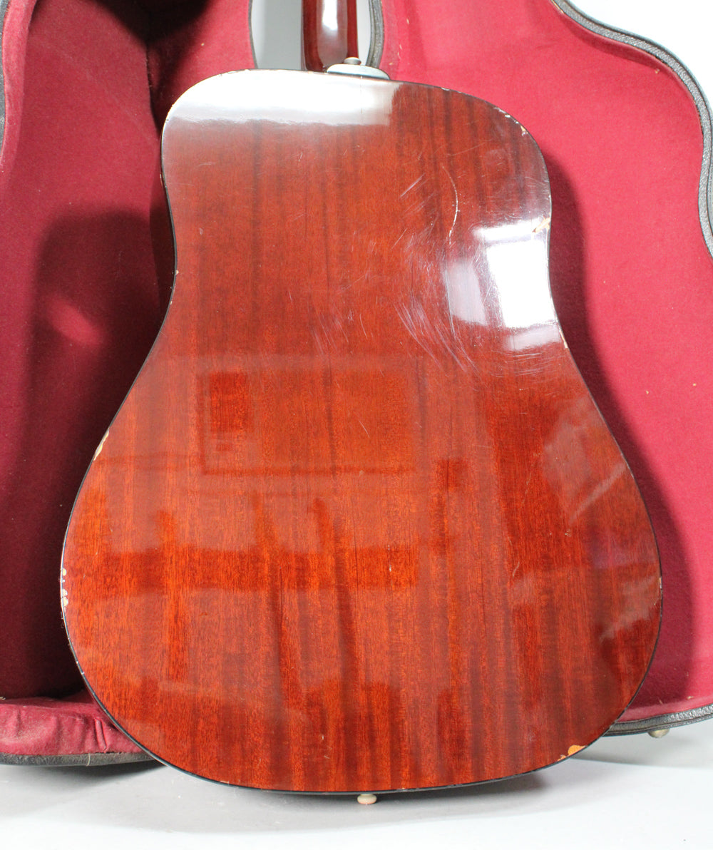 The guitar's dark reddish-brown back is shown, with many scratches and dings, especially on the lower bout and edges.