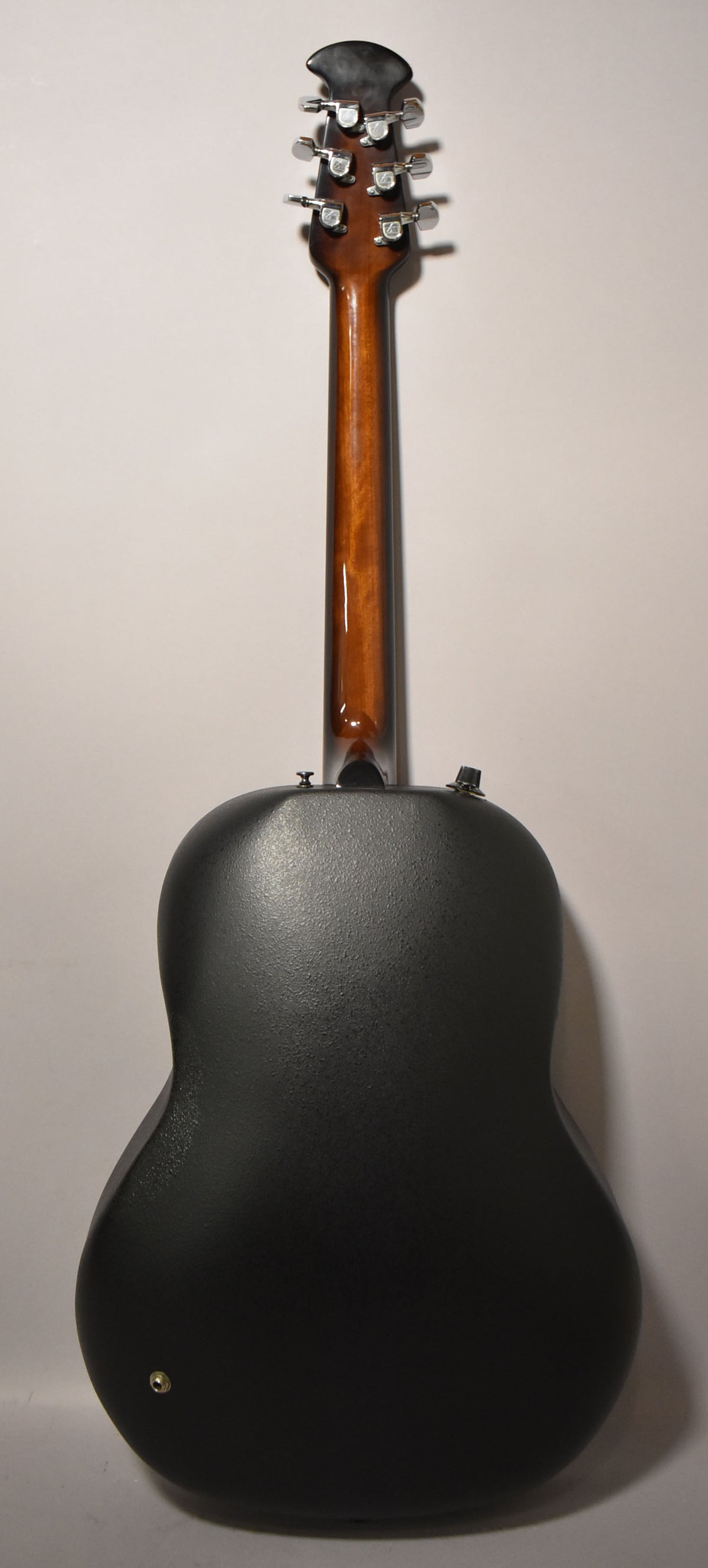 The guitar's back, showing a textured black composite body, a glossy brown neck, and chrome tuners on the headstock.