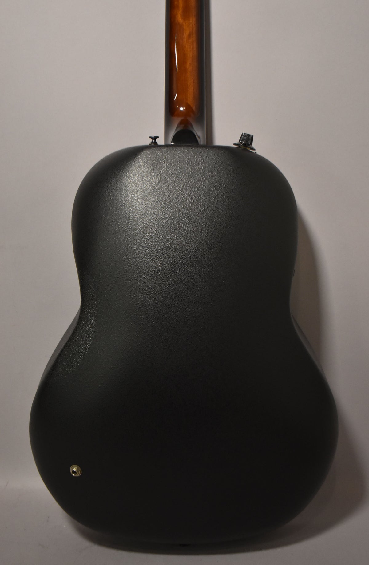 Rear view of the guitar's textured black composite bowl back, with a glossy brown neck extending upwards and a strap button at the bottom.