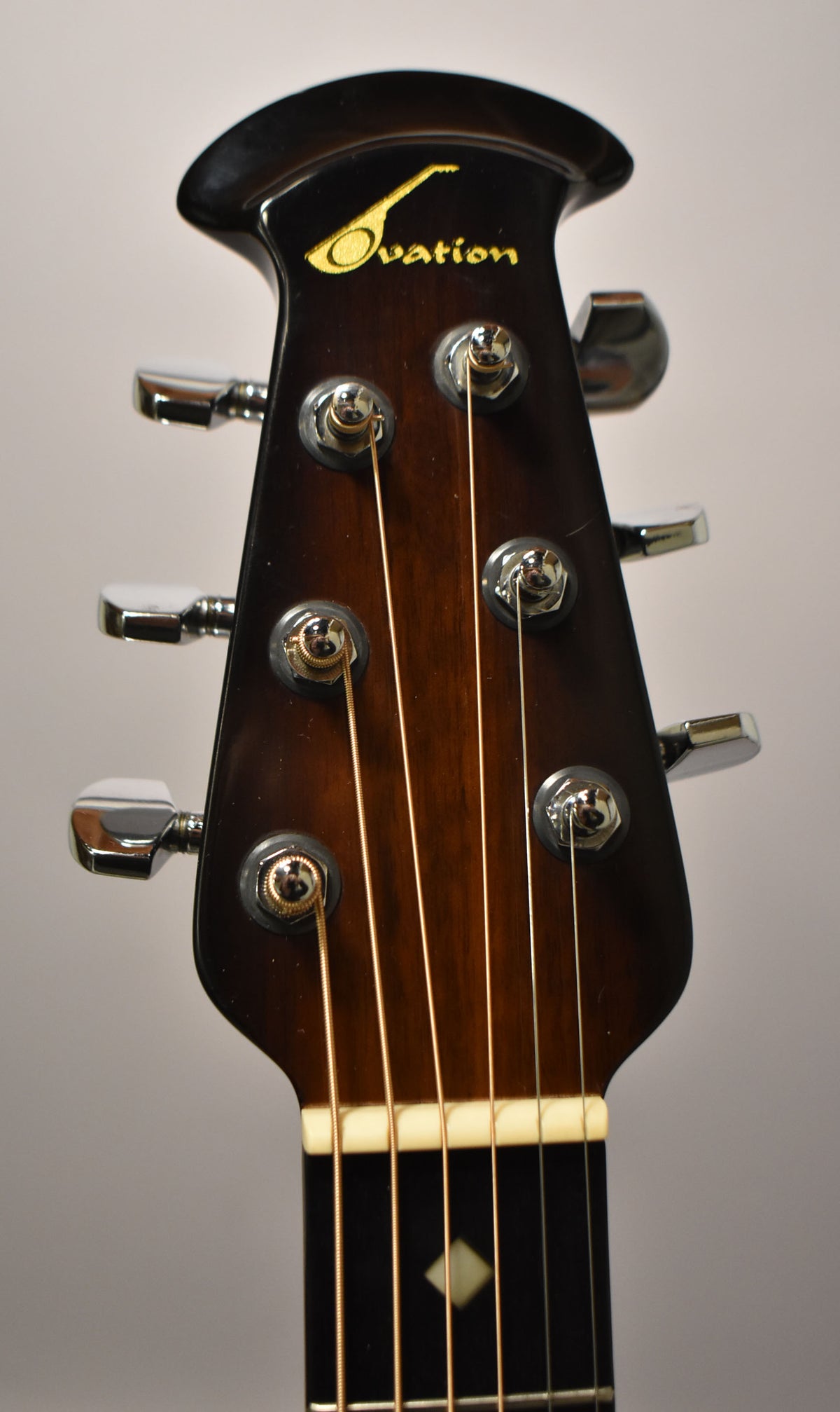 Close-up of the guitar's headstock, showing the dark brown sunburst finish, six chrome tuners, and the top of the fretboard with a diamond inlay.