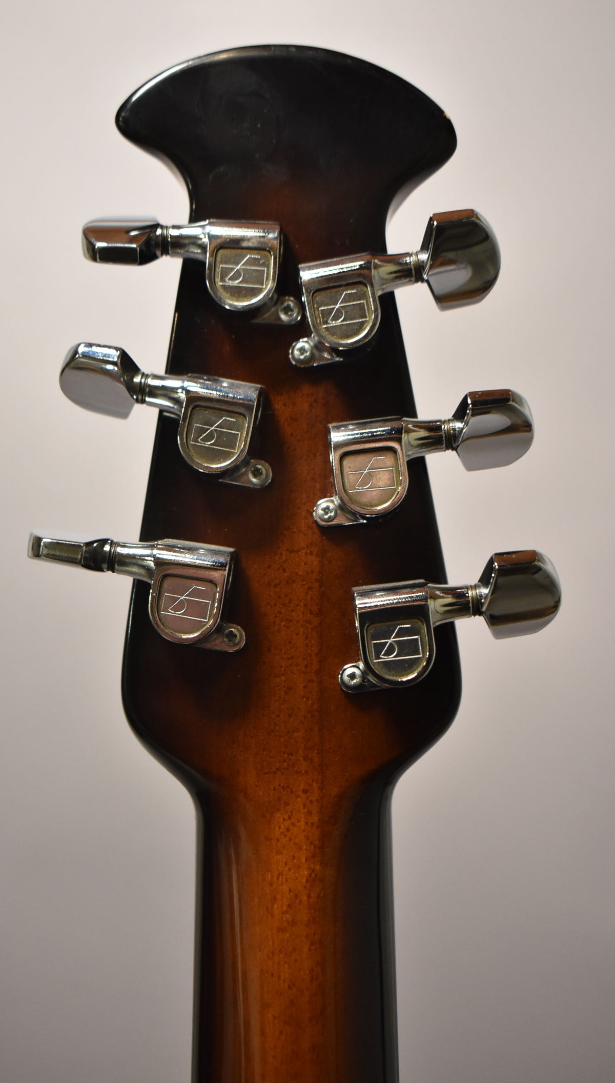 The guitar's sunburst headstock and neck are viewed from behind, showing six chrome tuners with light wear.