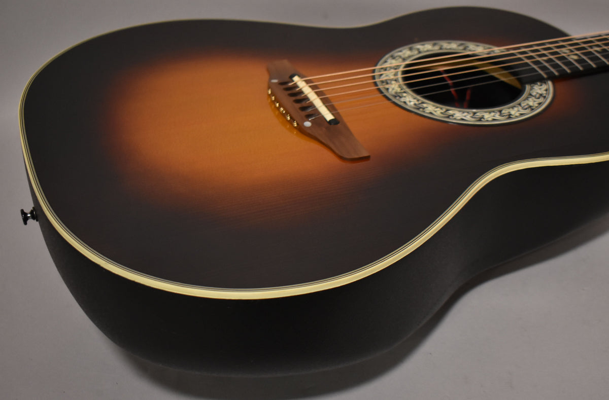 The sunburst acoustic guitar is angled to show its textured black bowl back, light binding, and ornate soundhole rosette.