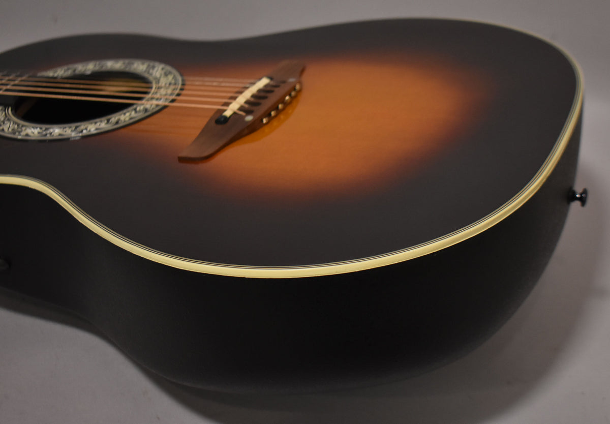The sunburst acoustic-electric guitar's body is angled, showing the dark brown back and sides, and the ornate soundhole.