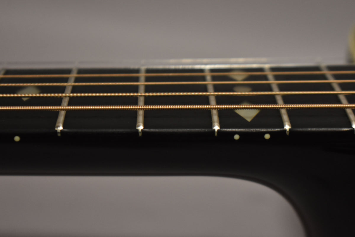 Close-up of the dark fretboard with diamond inlays, showing four frets and six bronze strings from the side.