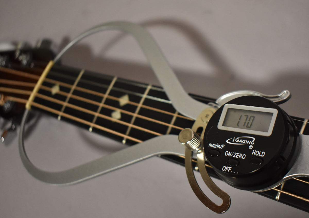 A digital caliper measures the nut width of the dark fretboard, showing "1.70" on its screen, with diamond inlays visible.