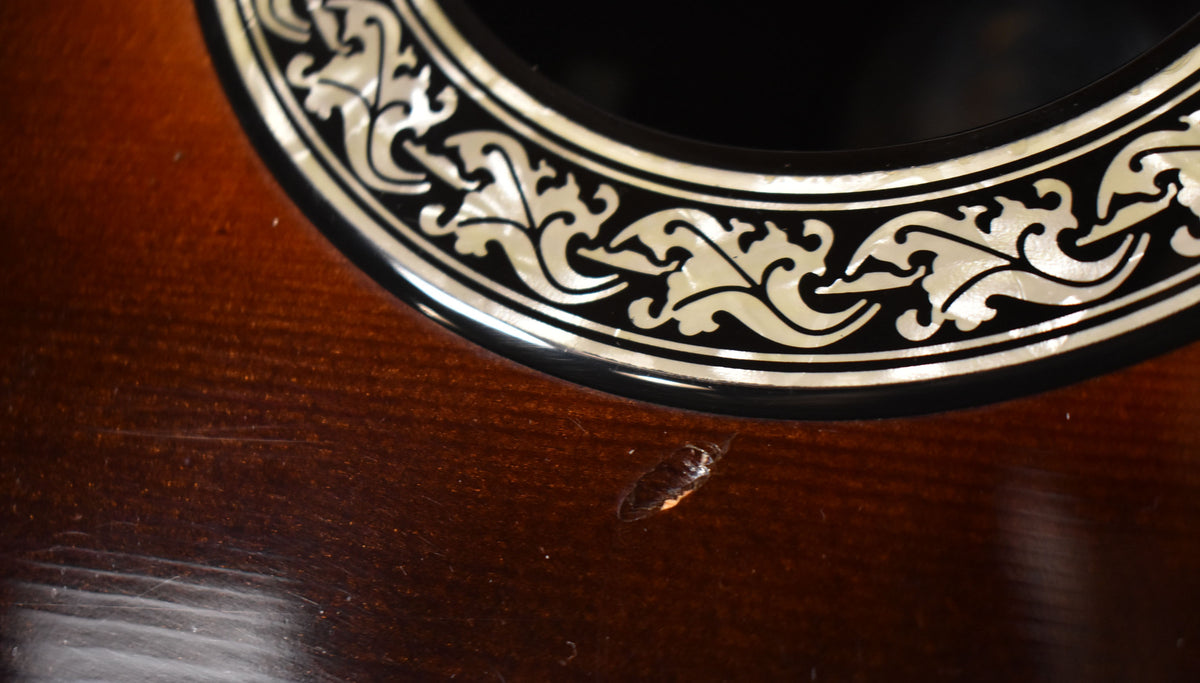 Close-up of the sunburst body, showing ornate mother-of-pearl rosette inlay and a small chip in the finish below the soundhole.