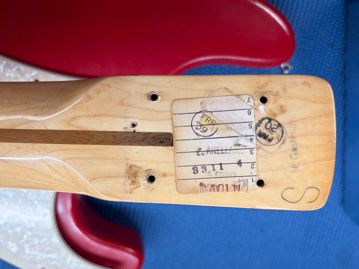 Close-up of the bass's natural wood neck heel, showing a worn paper label with numbers and text, and four screw holes.