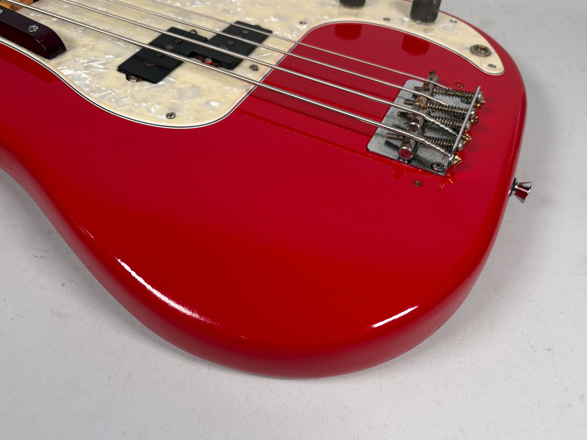 Close-up of the glossy red bass body, showing the pearloid pickguard, split pickup, chrome bridge, and strap button.