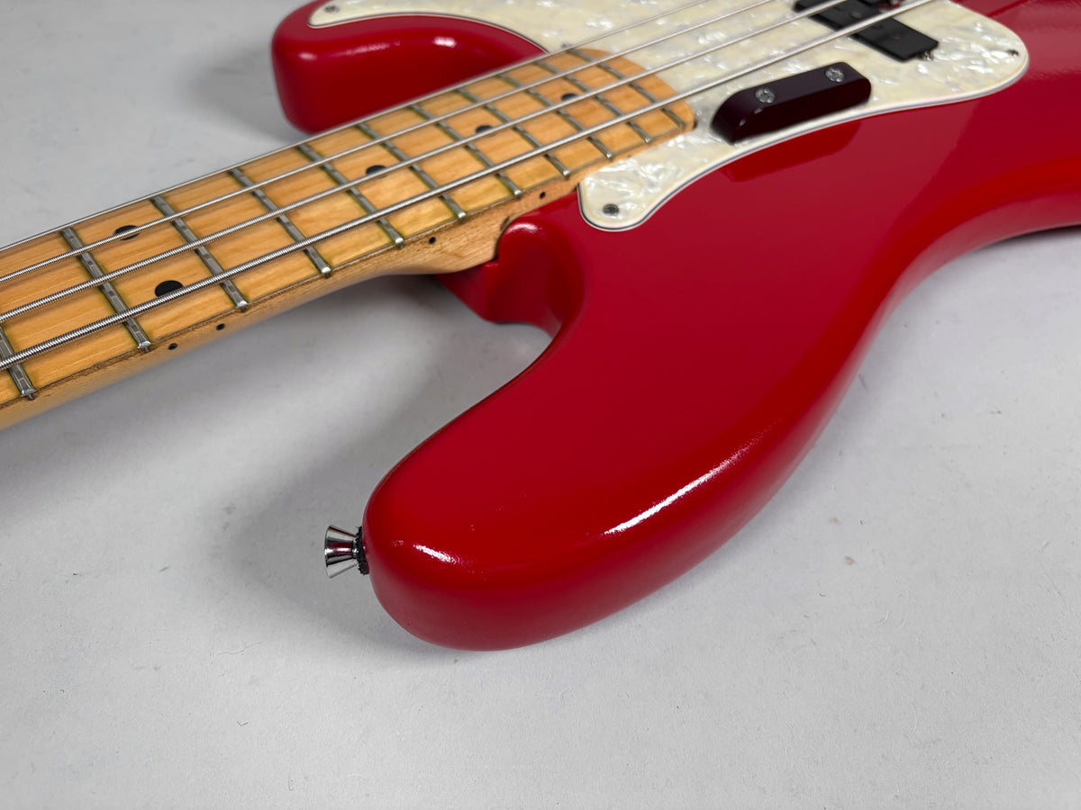 Close-up of the bass body in glossy Moroccan Red, showing the maple fretboard, pearloid pickguard, and strap button.