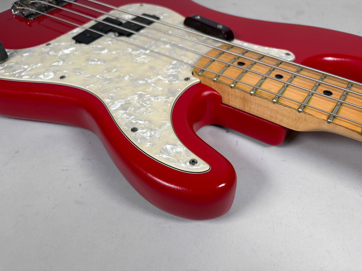 Close-up of the bass's lower body, showing the glossy red finish, pearloid pickguard, and maple neck with fretboard wear.