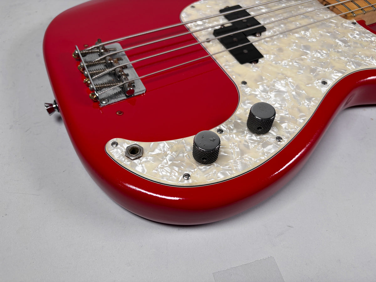 Close-up of the bass's lower body, showing the glossy red finish, pearloid pickguard, chrome bridge, and two knurled black control knobs.