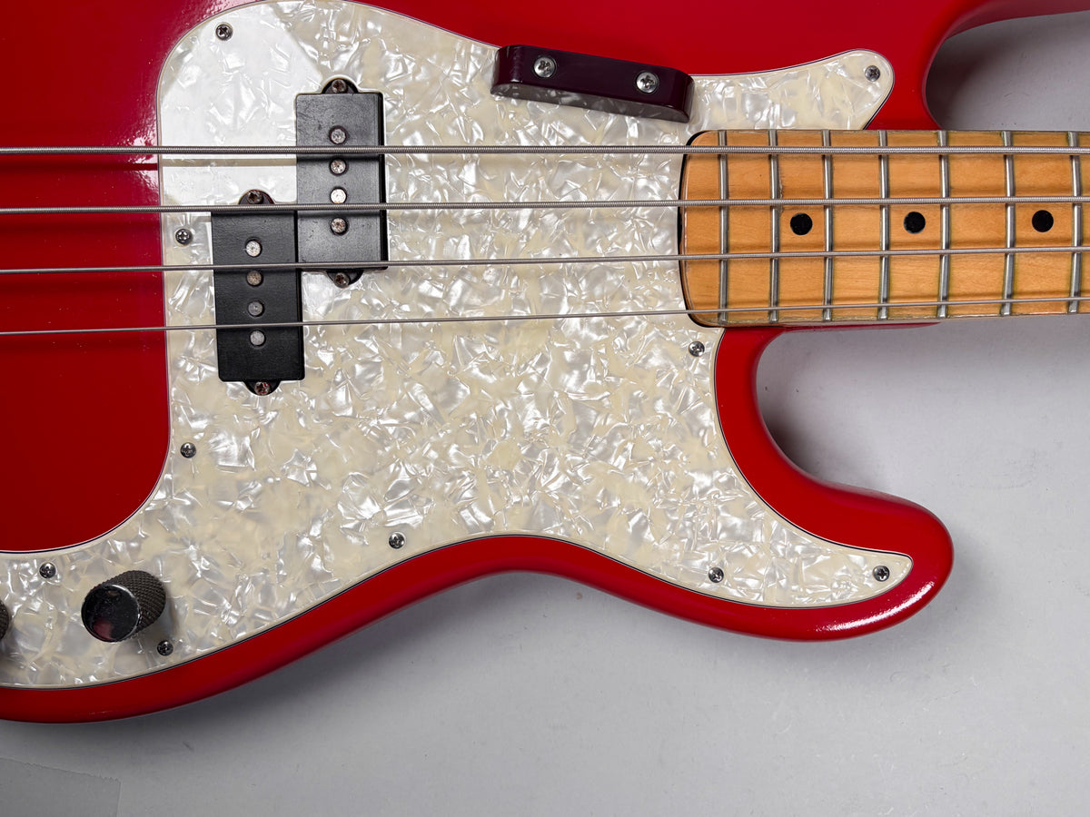 Close-up of a red bass guitar body with a pearloid pickguard, split pickup, and maple fretboard with black dot inlays.