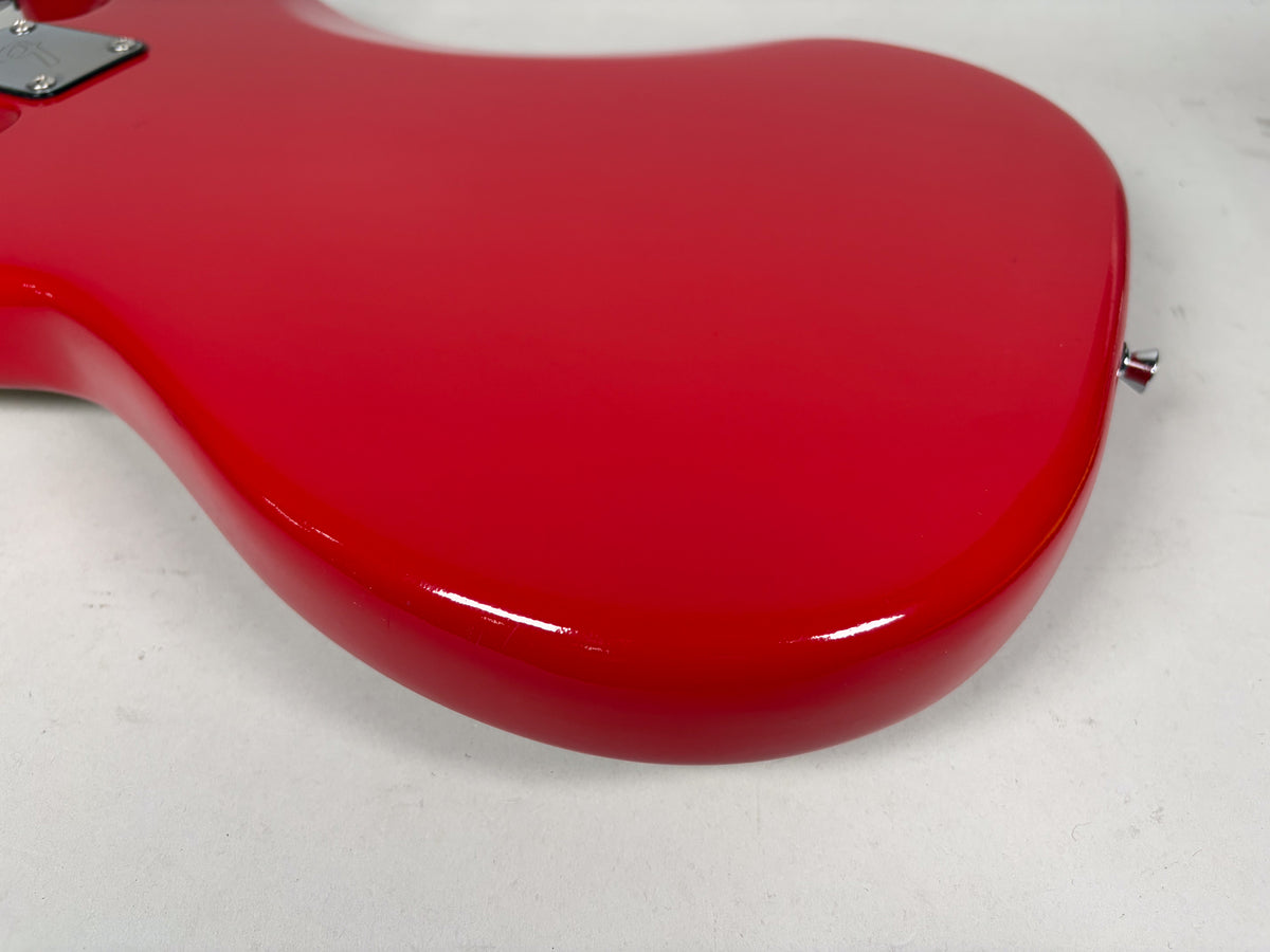 The bass's glossy red body is angled from the upper left, showing the lower bout and strap button, with minor scuffs on the finish.