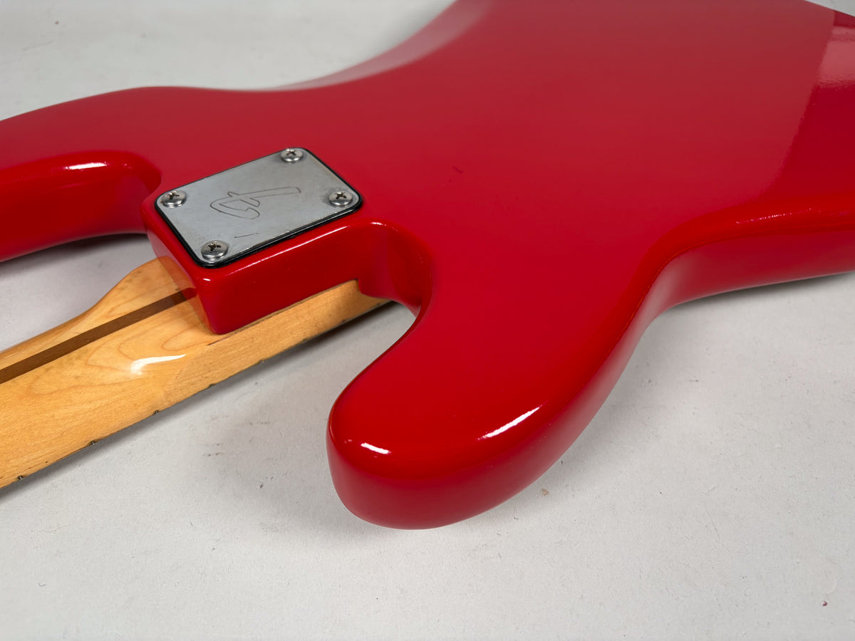 The bass's glossy red body and light wood neck meet at a four-bolt chrome neck plate, with minor wear visible on the body.
