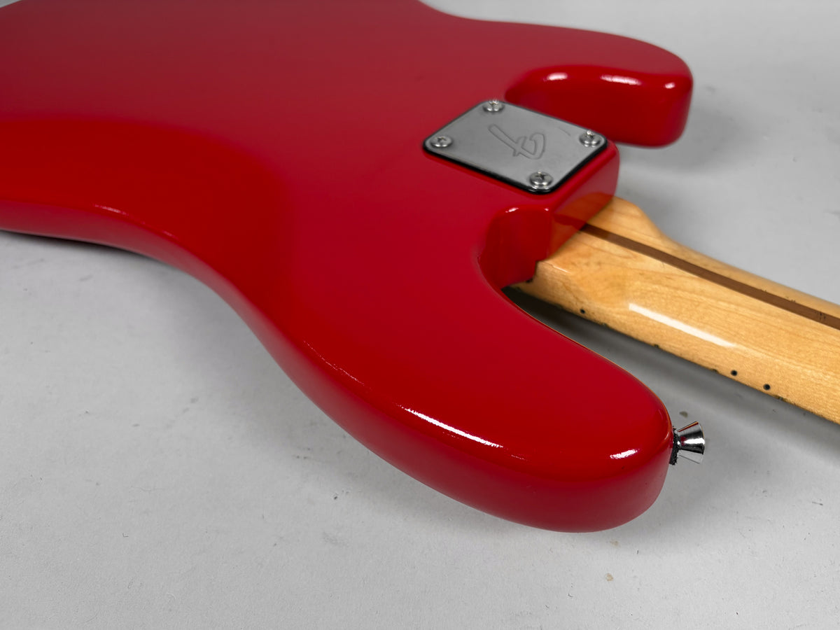 The bass guitar's glossy red body, with a chrome strap button, meets a light wood neck with a dark stripe and a silver neck plate.