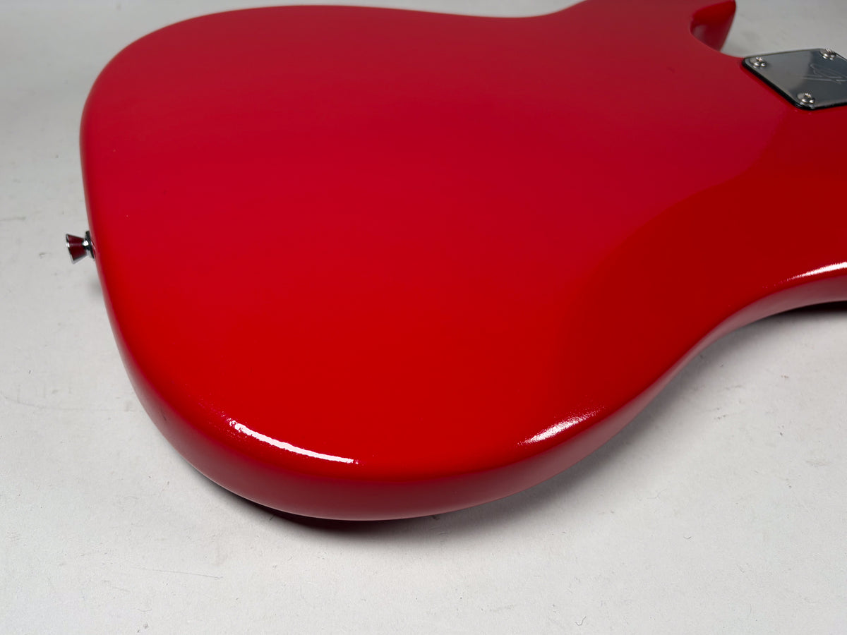 Close-up of the bass's glossy red body from the lower bout, showing a chrome strap button and the neck plate with some light wear.