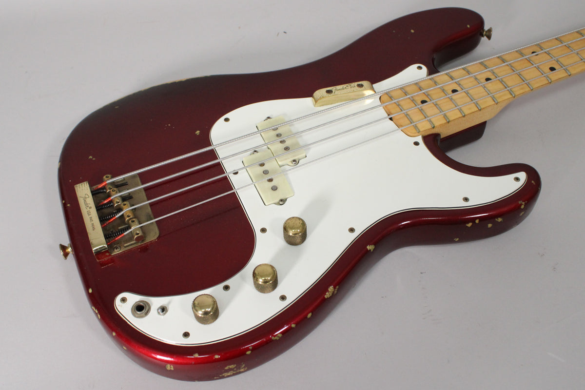 Angled view of a candy apple red bass with a white pickguard, gold hardware, and significant paint chipping along the body edges.