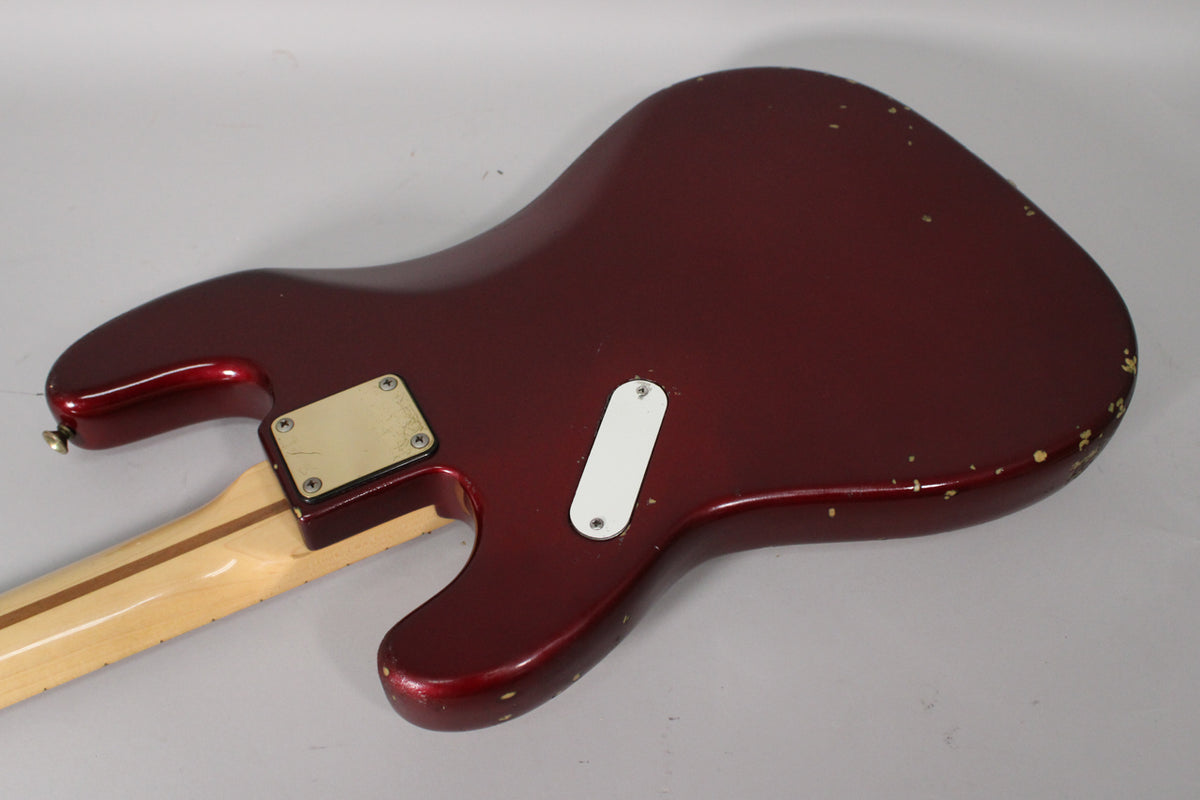 Rear view of the candy apple red bass body, showing a white control plate, a gold neck plate, and significant paint chipping.
