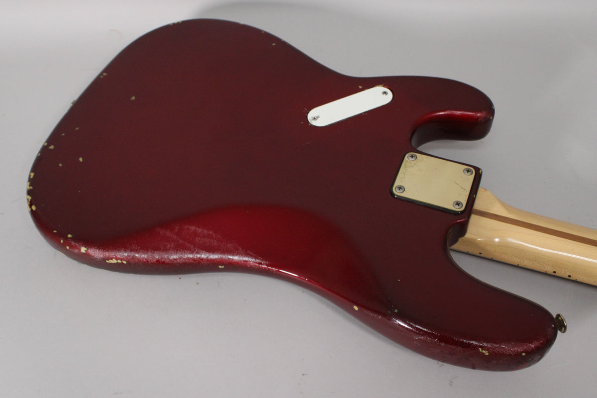 The bass's candy apple red body, viewed from the back, shows significant finish wear and chips, revealing a lighter undercoat.