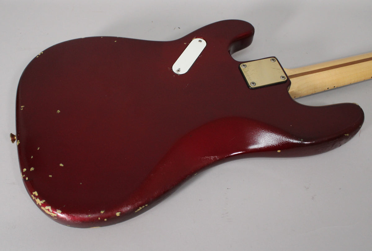 The back of the candy apple red bass body shows significant paint chipping along the bottom edge, with a white control plate and gold neck plate.