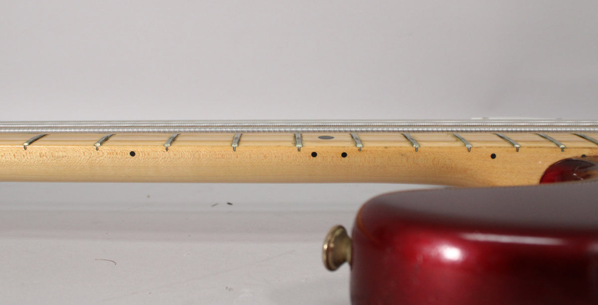 Close-up of the bass neck from the side, showing the maple fretboard with dot inlays and a small chip near the body.