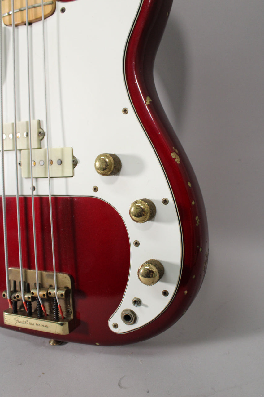Close-up of the bass body, showing the candy apple red finish with many chips, white pickguard, gold hardware, and three gold control knobs.