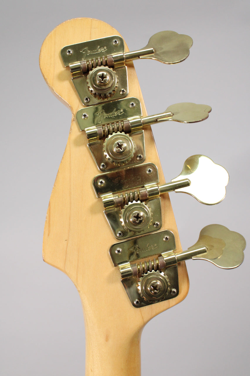 The bass headstock, angled slightly, features four gold-plated cloverleaf tuners on a light wood finish, showing minor wear.