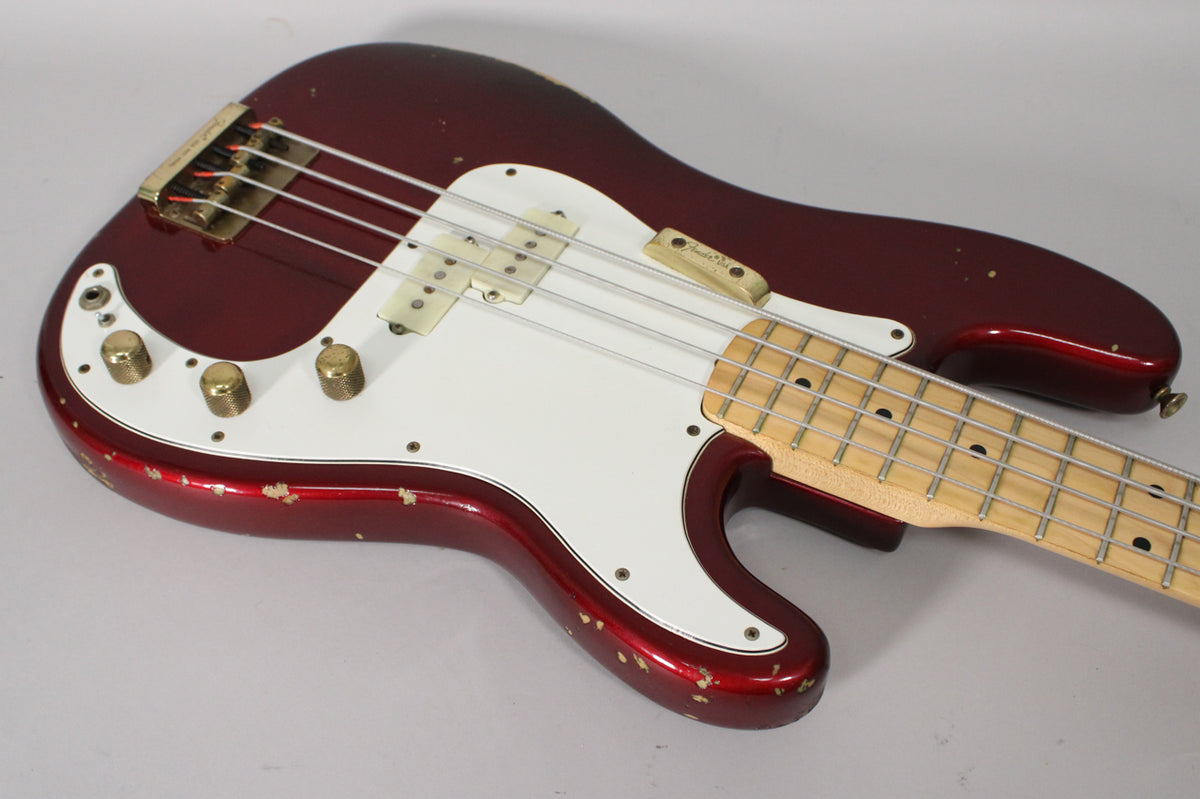 The candy apple red bass body, with a white pickguard and gold hardware, shows significant paint chipping and wear.