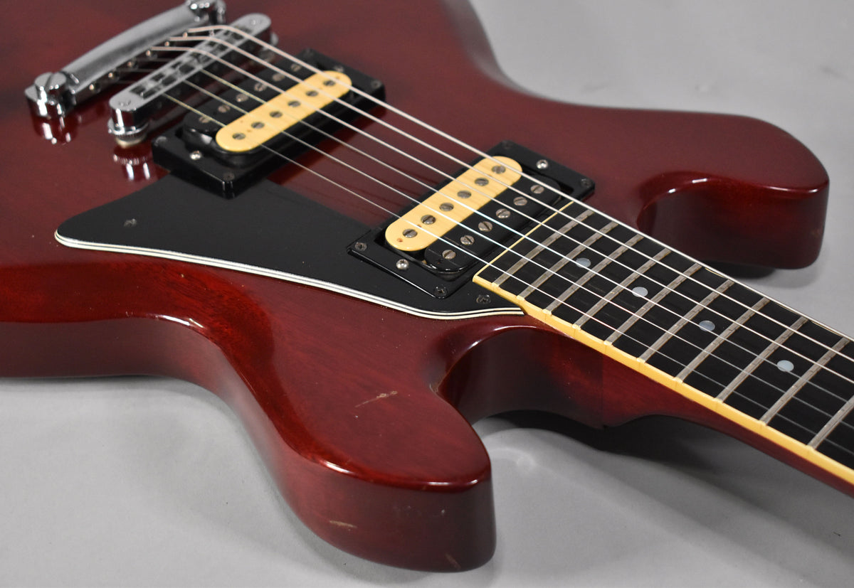Close-up of the cherry red body and fretboard, showing two cream-colored humbucker pickups, a black pickguard, and light wear.
