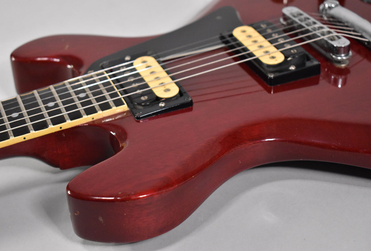 Close-up of the cherry-finished body and neck, showing two cream humbucker pickups, black pickguard, and minor dings on the lower bout.